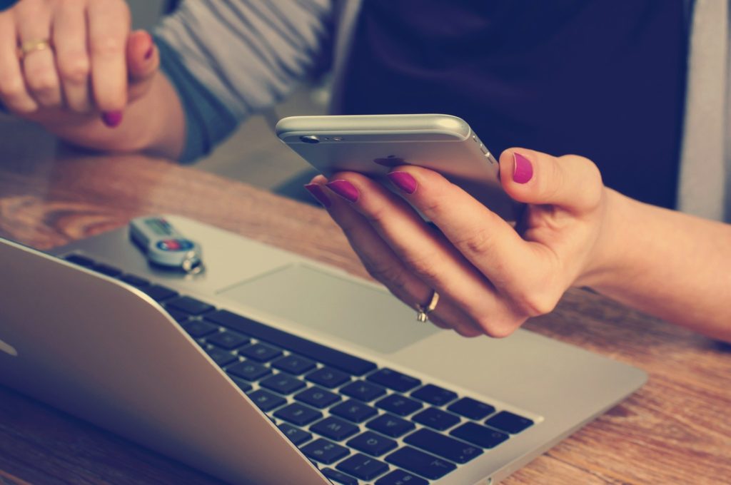 Woman's hand holding smart phone and using computer.